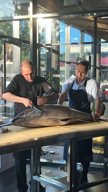 Zwei Köche filetieren einen ganzen Yellowfin-Thunfisch auf einem Tisch bei einer Live-Zerlegung im Restaurantbereich.