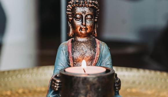Im Moment ankommen & Kraft schöpfen Buddha-Figur, die ein Teelicht hält.