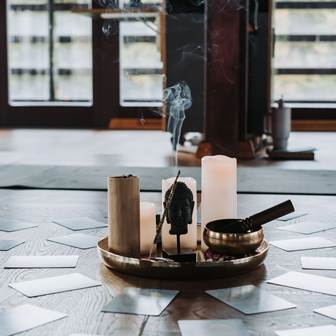 Hier schaffen Sie Raum für innere Ruhe Ein Tablett mit Kerzen, einer Klangschale und Räucherstäbchen. Rundherum liegen Karten.