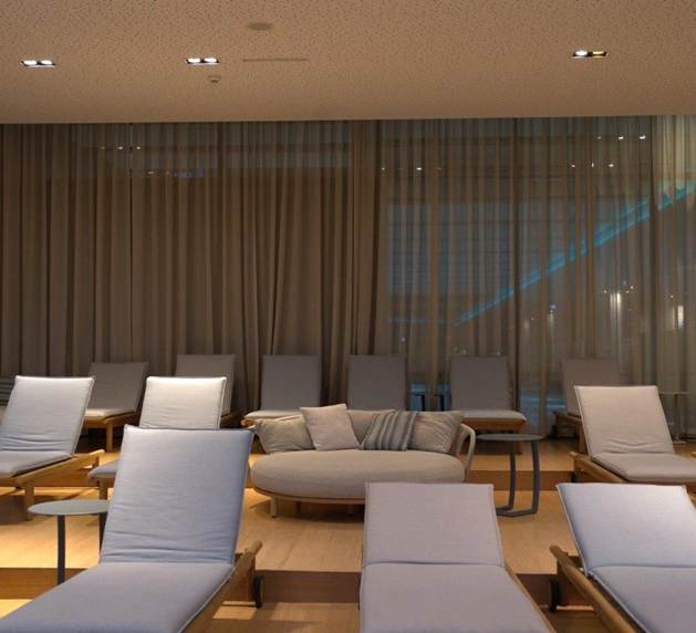 Ruheraum mit Liegenreservierung im Premium Day Spa Linsberg Asia Ruheraum mit mehreren gepolsterten Liegen, Sitzmöbeln und Beistelltischen vor bodentiefen Vorhängen.