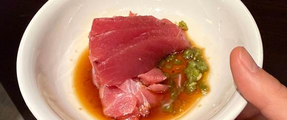 Kleine weiße Schale mit rohem Thunfisch in Sojasauce und grüner Wasabipaste, gehalten in einer Hand