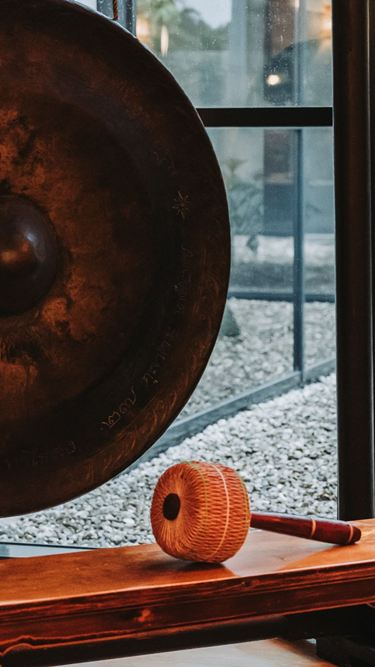 Harmonie für Körper und Seele Ein Gong und zwei Buddha-Statuen davor.