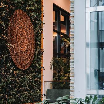 Genießen Sie ein sinnliches Schönheitsritual Eine bronzefarbene Mandala-Skulptur, umgeben von Pflanzen, an der Wand.