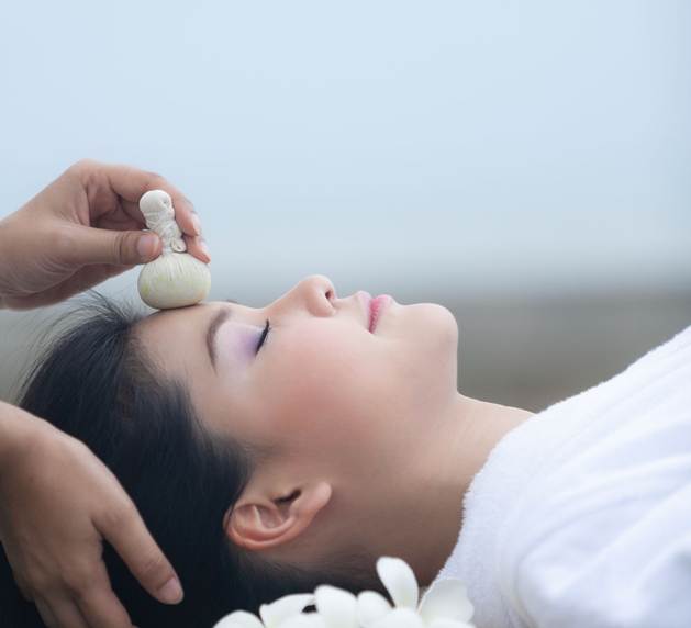 Traditionelle thailändische Kräuterweisheit vereint mit moderner, sanfter Pflege Eine Frau bekommt eine Gesichtsbehandlung.